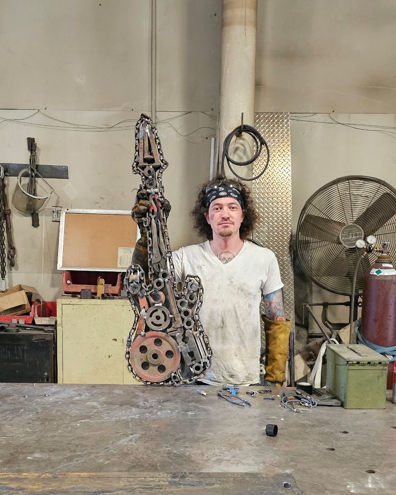 The artist in his shop, holding a guitar welded from chains, gears and scrap steel